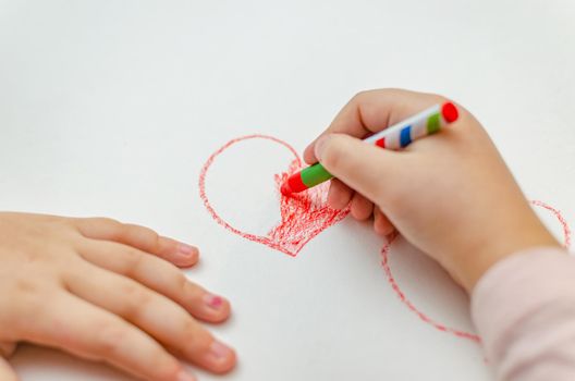A little girl is drawing a heart with red chalk - high angle image with selective focus. Valentine's day concept.