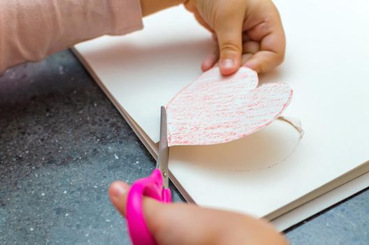 The girl's hand holds a heart cut from paper. Children's creativity - drawings and crafts for Valentine's Day or Mother's Day