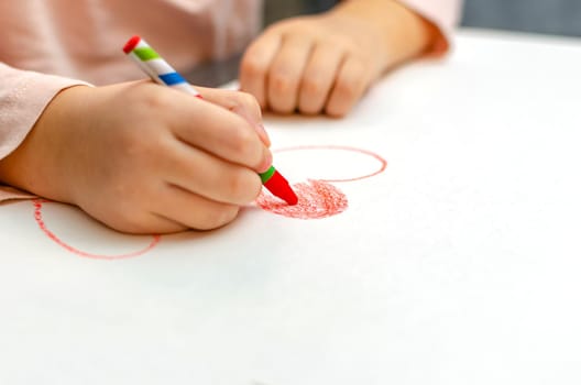 A little girl is drawing a heart with red chalk - high angle image with selective focus. Valentine's day concept.