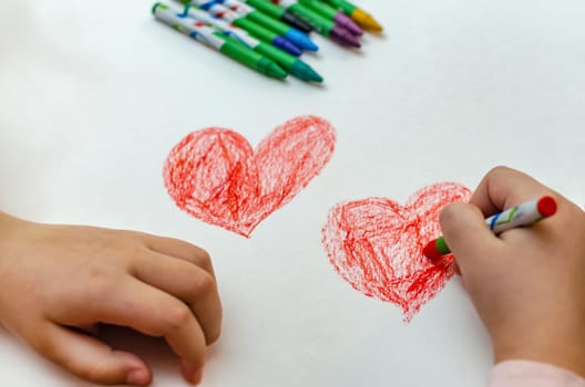A little girl is drawing a heart with red chalk - high angle image with selective focus. Valentine's day concept.