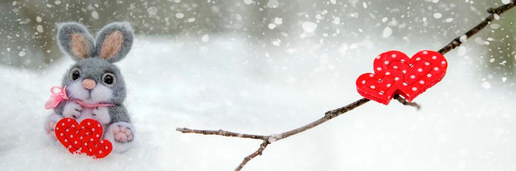 Happy Valentine's Day greeting card or banner. Red hearts on a branch of a snow-covered tree in winter. Holidays Happy Valentine's Day. Snowfall on the background of the forest.