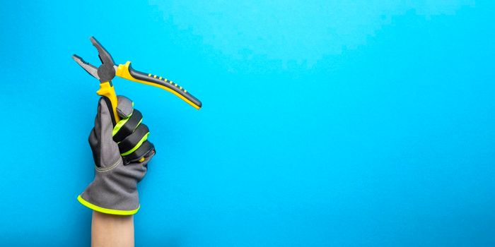 Pliers. Yellow and black pliers in the hand of an electrician on a blue monochrome background. Repair and installation tool. Banner for the design and printing of construction topics