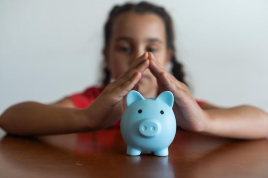 Smiling little girl posing with a piggy bank in her hands, standing against a blue background in a studio with free space. Family savings.