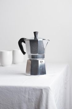 Classic aluminium coffee maker on white table with coffee space