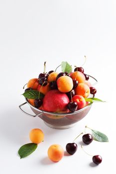 apricots and cherries in a metal bowl on a white background. Copy spase