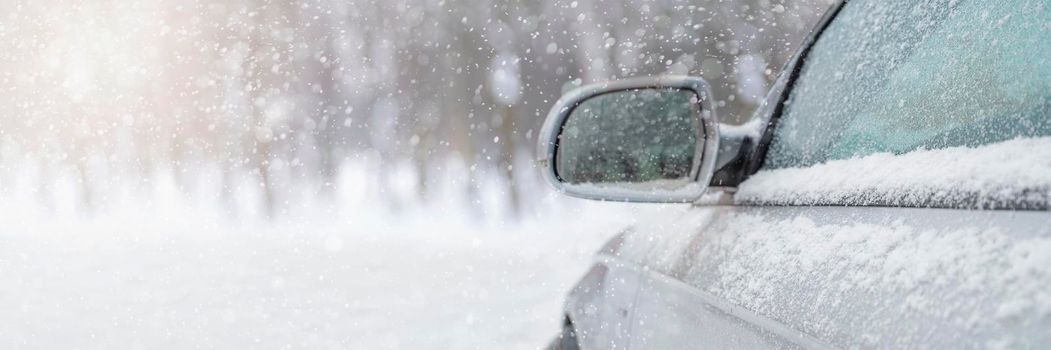 The car drives through the snow, the bright winter sun shines against the background of the forest. Close-up rearview mirror. The vehicle is covered with snow