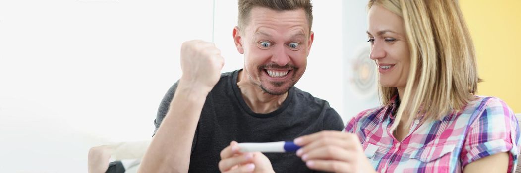 Portrait of happy husband got news about wifes pregnancy, waiting for baby, cheerful man show yes gesture. Woman holding positive pregnancy test. Family growing, happiness concept