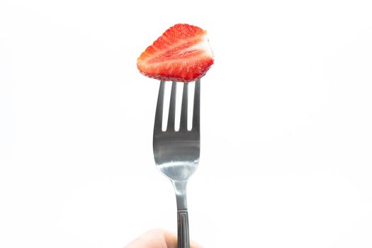 Half of a ripe juicy red strawberry on a metal fork on a white background.