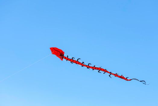 Flying kite. Colorful kite flying in the wind in the blue sky among the clouds. Long serpent in the form of a red dragon.
