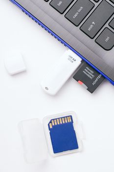 MicroSD memory card with adapter, white USB stick plugged in the ports of the modern blue laptop