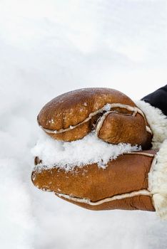 First snow, making snowballs in the park close-up. Hands in warm mittens make snow in winter. Brown leather mittens in the snow in winter