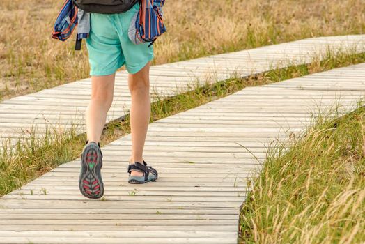Wooden path in the mountains. Winding tourist path made of boards in the mountains. Legs of a young guy 10 years old close-up go to the mountains along a tourist route with a backpack.