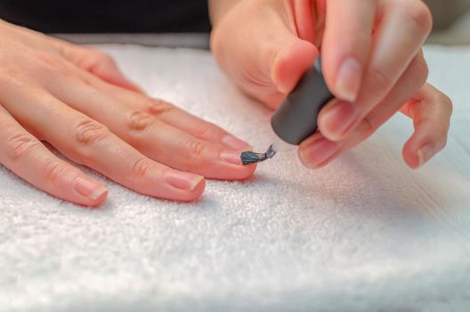 A woman applies a primer to her nails before applying varnish. Close-up of a hand