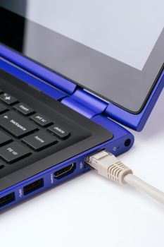 White LAN Internet cable plugged in  the port of a modern blue laptop