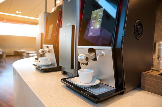 A beautiful sun glare falls on self-service coffee steam machines with white ceramic coffee cups in a VIP lounge restaurant or cafeteria in an international airport departure terminal