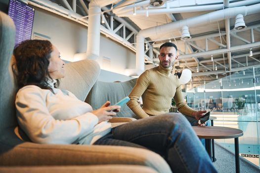 Beautiful newlyweds on honeymoon trip, man and woman chat while relaxing in the VIP lounge of the departure terminal of the international airport, waiting to board the flight. Air travel concept