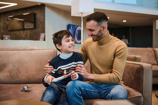 Handsome loving young father gently hugging his son playing with toys planes while waiting for customs and passenger control before boarding the flight in the international airport departure terminal