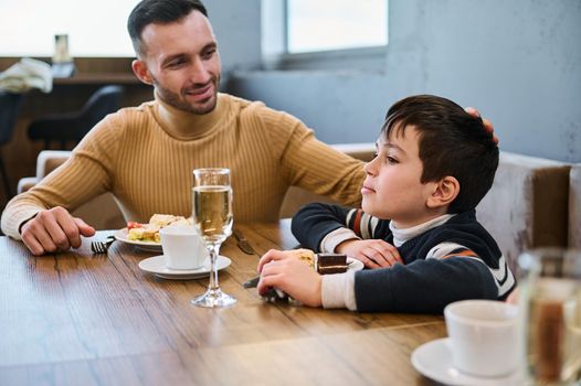 Adorable Caucasian school age child boy with his father having lunch together at cafeteria