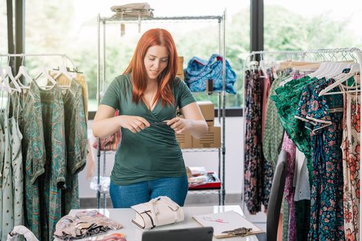 young businesswoman, taking photos of a garment in her office with her smartphone for her online clothing shop. woman owner of a small online business. work and business concept. background with clothes racks and clothes.