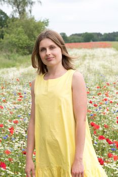 a beautiful young blonde woman in a yellow dress stands among a flowering field of poppies, daisies, cornflowers and laughs. High quality photo