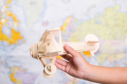 Close-up of wooden toy plane in children's hands on world map background in kids room at home. Childhood dream imagination and Travel concepts.