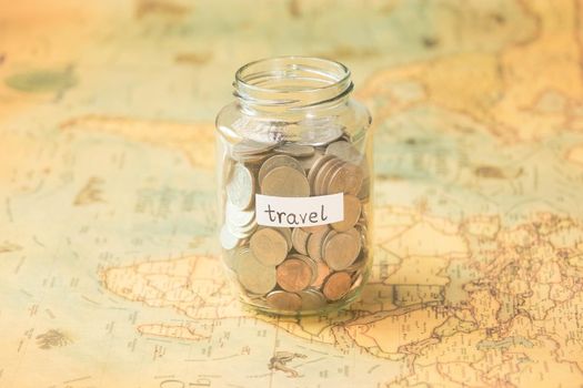 Glass jar with coins and travel inscription on world map on table. Travel concept and saving money.