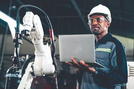 African American factory worker working with adept robotic arm in a workshop . Industry robot programming software for automated manufacturing technology .