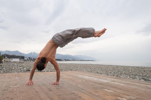 Shirtless caucasian man doing backflip on pebble beach