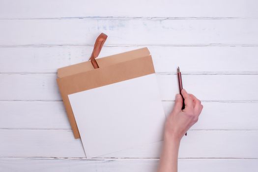 One Craft envelop, white paper and ink pencil in hand on white wooden background