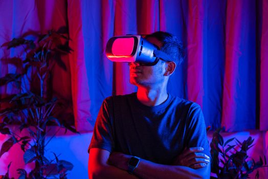 Asian handsome man wear VR helmet excited emotional at home purple and blue background, experiencing virtual reality goggles experiencing reality excited emotional, metaverse and cyberspace