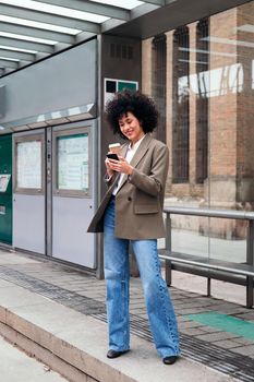 young latin woman waiting at the tram stop checking her mobile phone, concept of urban and modern lifestyle