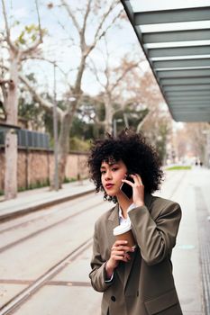 young latin business woman talking on the phone while waiting at the tram stop, concept of communication and urban lifestyle