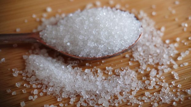 Macrophotography.A spoon with sugar on a wooden table. Close-up of sugar crystals.Background or texture