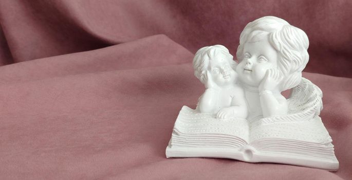 Plaster statuette of little lying angels reading a big book. Details and portrait.Space for text.Background or texture