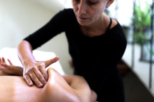 Latina massage therapist hand massaging shoulder blade. Wellness concept.