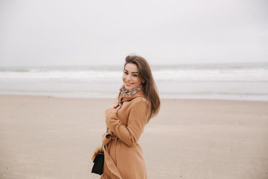 Portrait of beautiful woman walkink along the coast near the north sea. Elegant lady in brown coat with fashion make up stand in front of the sea.