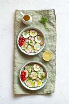 radish and cucumber salad served in a two bowls on the linen napkin and decorated with red currants, top view