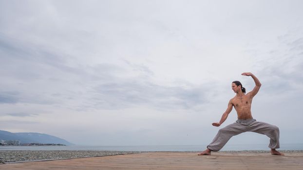 Caucasian man with naked torso practicing wushu on the seashore