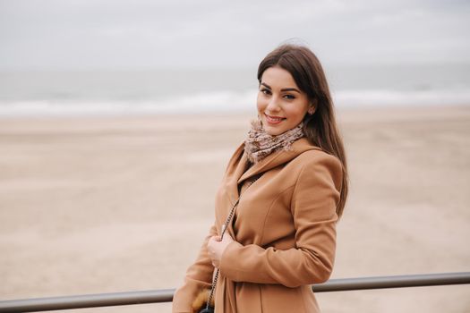 Stylish lady with make up in beautiful coat standing along North Sea. Woman smile.