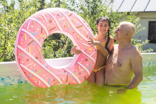 grandfather and granddaughter swimming in the pool in the garden near the house.
