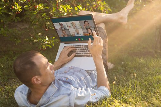 Young man in the garden in summer on the laptop computer while chatting online as a freelancer