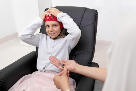 Portrait of a smiling girl siting on a chair of a clinic during biofeedback therapy