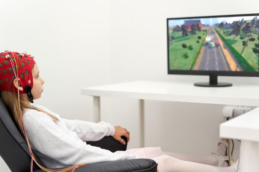 Girl sitting on a chair while wearing headgear to monitoring the brain activity during a biofeedback session