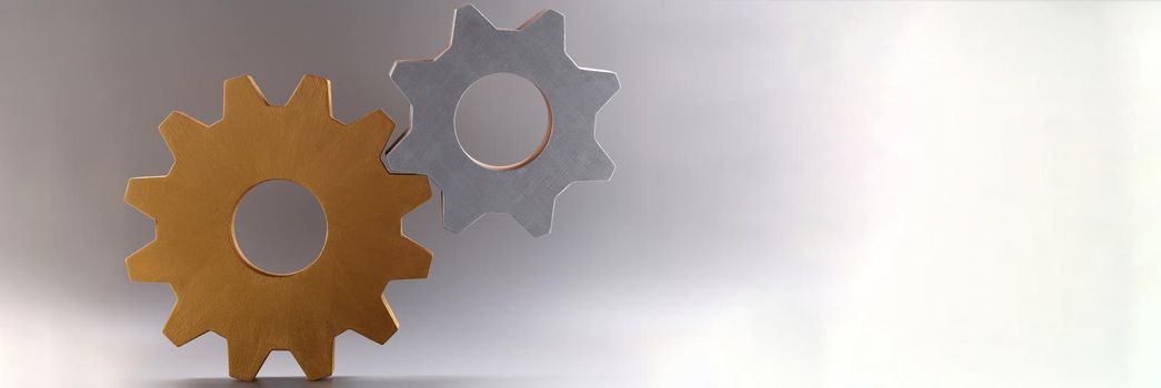 Closeup of golden and silver connected gears on gray background. Teamwork concept