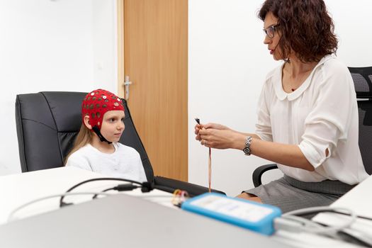 Female doctor with electrodes on her hands to put a girl through biofeedback session