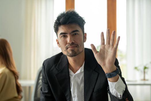 Webcam portrait of asian businessman looking directly at camera with friendly smile, waving hand, greeting gesture.