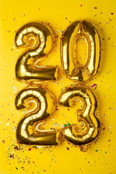 2023 concept Happy New Year from golden foil balloon on yellow background