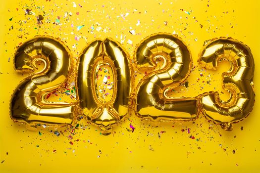 2023 concept Happy New Year from golden foil balloons and confetti on yellow background
