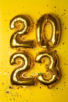 2023 concept Happy New Year from golden foil balloon and confetti on yellow background stock photo