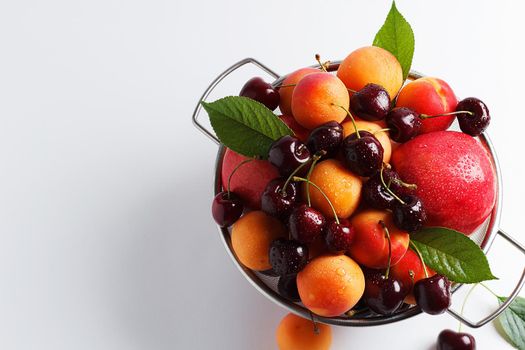 apricots and cherries in a metal bowl on a white background. Copy spase